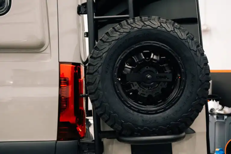 Full-size spare tire mounted on an Owl Vans rear door tire carrier on the back of a Mercedes-Benz Sprinter conversion.