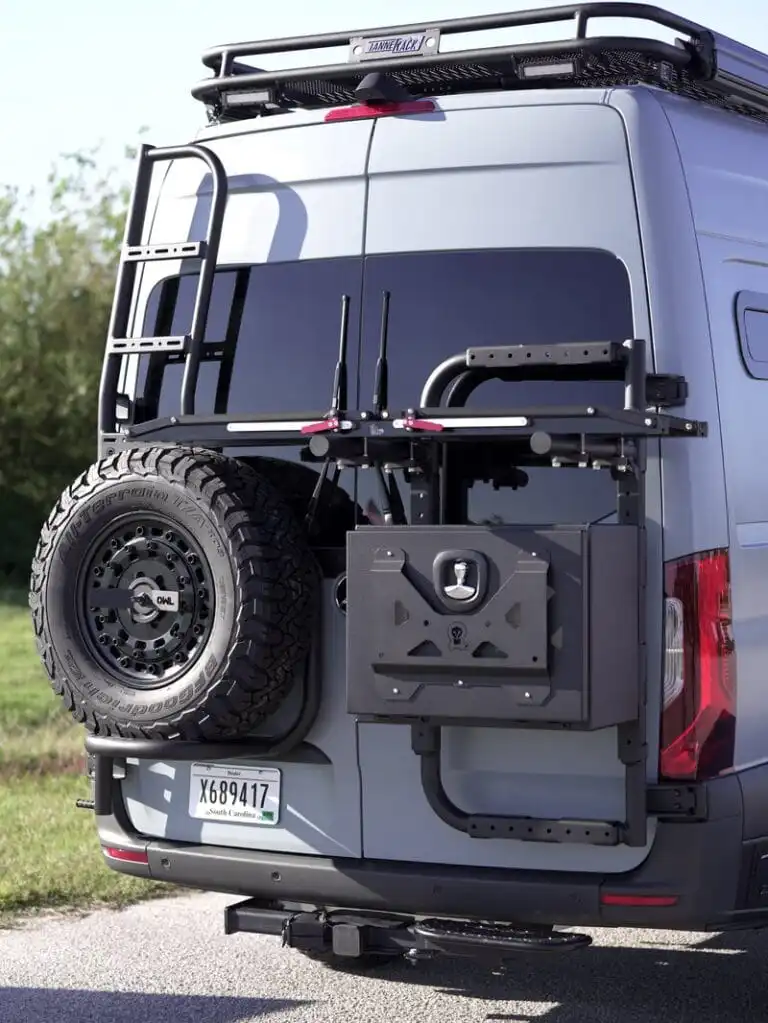 dsc06576 - Patrol Vans Rear of a gray van with a mounted spare tire on the left and a fold-out heavy-duty bike rack attached to the tailgate, plus a metal cargo box on the back.