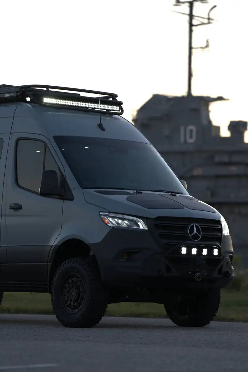 dsc06608 - Patrol Vans - Patrol Vans Gray Mercedes-Benz van outfitted with a roof rack and LED light bar, parked on a road with a large ship in the background