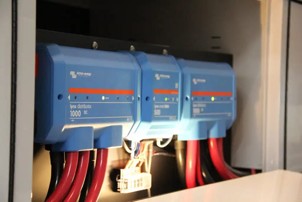 Blue Victron energy Lynx distributor modules mounted in an electrical cabinet with thick red and black cables and status LEDs nearby.