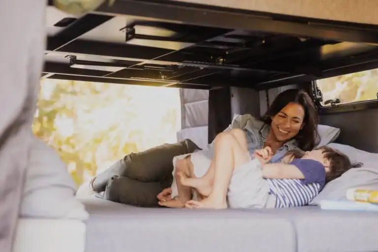 Mother and child cuddling on a bed inside a camper van, smiling and enjoying a cozy moment.
